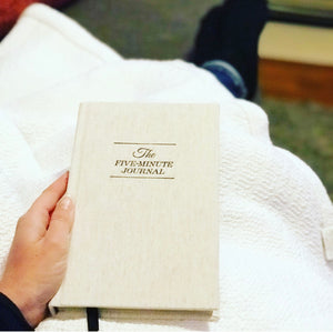 The Five Minute Journal by Intelligent Change resting on white blanket and couch